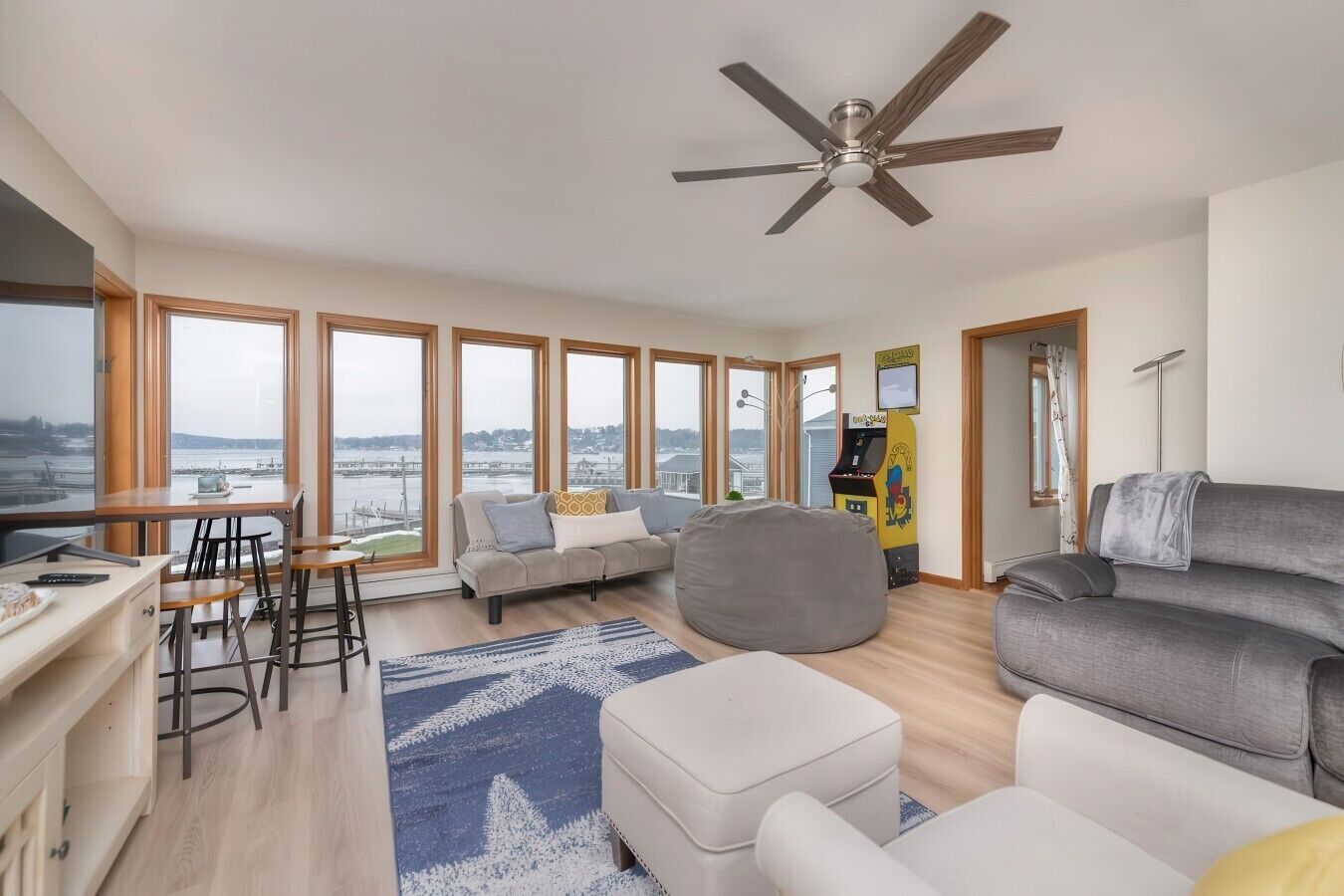 Ein modernes Wohnzimmer mit großem Fenster, Deckenventilator, Sofa, Sitzsack, Couchtisch und kleinem Fernseher.
