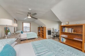 Camera da letto con due letti, una ventola a soffitto, una scrivania con sedia, una libreria e una finestra con persiane.