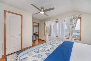 Une chambre à coucher avec un lit, un ventilateur de plafond, une fenêtre avec des rideaux et une vue sur la mer.