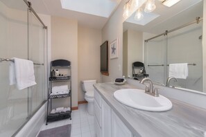 Un bagno moderno con box doccia in vetro, lavandino bianco su piano di marmo e uno specchio grande.