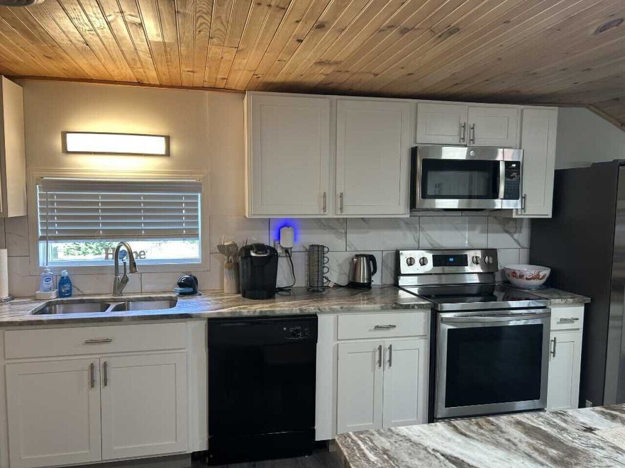 A modern kitchen with white cabinets, a stainless steel microwave, an oven, and a dishwasher.