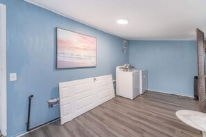 A laundry room with a white dryer, a washing machine, and a large painting on the wall.
