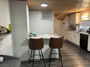 A kitchen with a bar area, wooden ceiling, white cabinets, and a window with blinds.