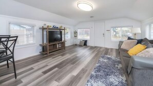 A spacious living area with a flat-screen TV on a wooden stand, a grey sofa with yellow cushions, and a patterned rug. - 2BR Shoreside Retreat w/ Beach Access & Interiors (Rochester)