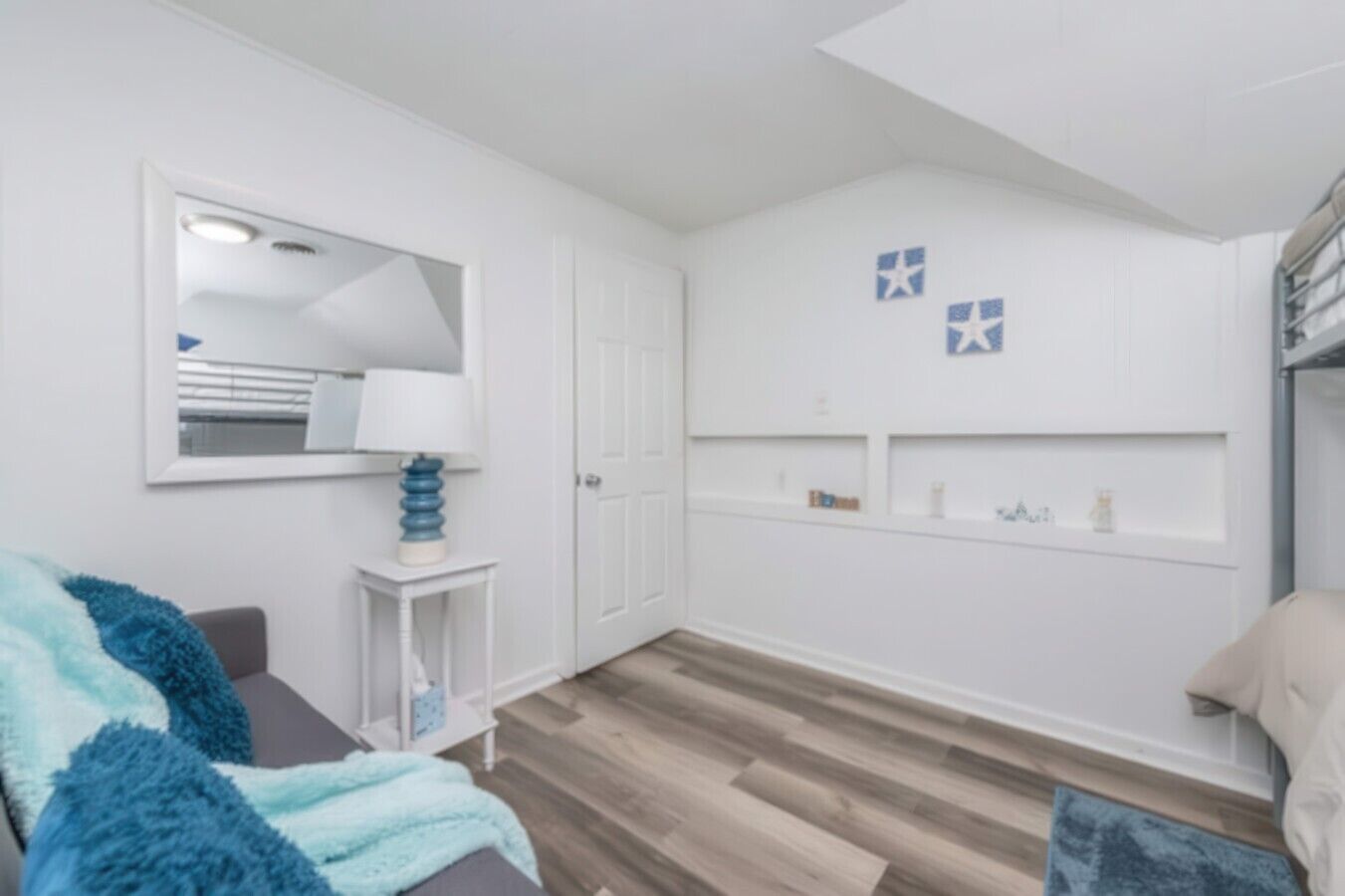 A room with a bed, a bedside table, a mirror, a wardrobe, and a shelf with decorative items.