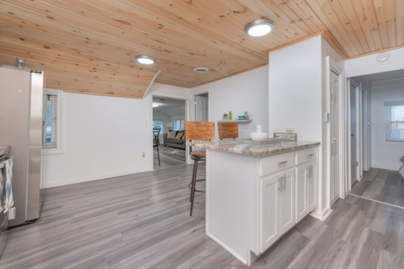 A modern kitchen with white cabinetry, a wooden ceiling, and a grey floor.