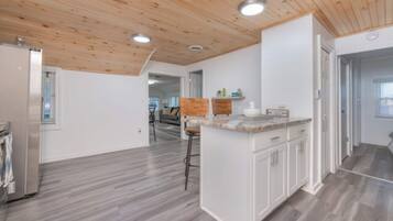 A modern kitchen with white cabinetry, a wooden ceiling, and a grey floor.