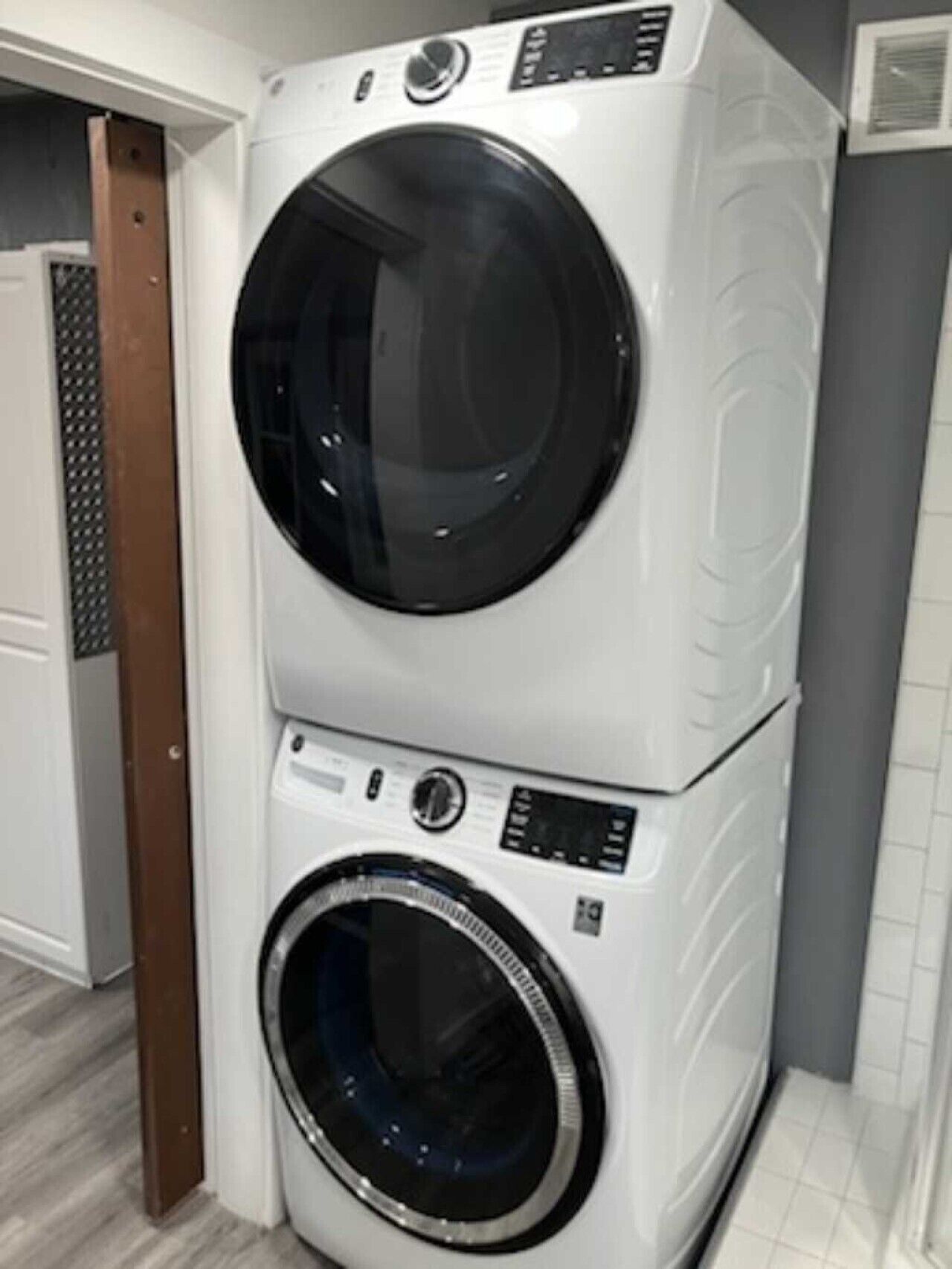 A stacked washer and dryer unit in a room with a wooden door and tiled flooring.