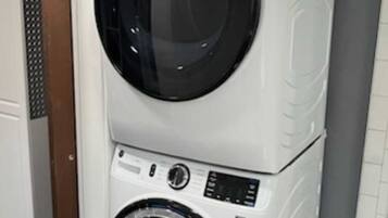 A stacked washer and dryer unit in a room with a wooden door and tiled flooring.