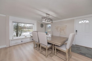 A dining area with a wooden table and four chairs, a world map on the wall, a clock, and a door with a window. - Waterfront Sodus Gem w/ Dock, Game Loft, Bay View (Sodus Point)