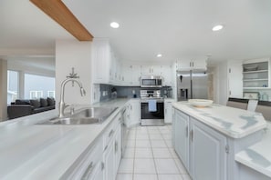 Une cuisine moderne avec des meubles blancs, des appareils en acier inoxydable et un grand îlot central doté d’un évier.