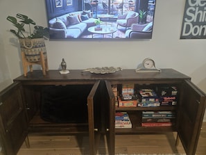 A wooden entertainment center with a television above it, a clock, and a shelf with board games. - Modern 2BR Retreat Near Downtown Birmingham (Birmingham)