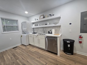 A compact kitchen with white cabinetry, a dishwasher, a sink, and a window with blinds. - Modern 2BR Retreat Near Downtown Birmingham (Birmingham)