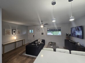 Una sala de estar moderna con un sofá, una mesa de comedor y un televisor montado en la pared.