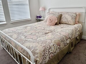 Een slaapkamer met een bed, een nachtkastje, een lamp en een raam met jaloezieën.