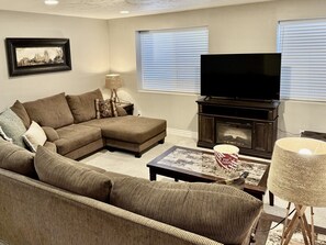 Una sala de estar con un sofá modular, un televisor de pantalla plana, una chimenea y una lámpara.