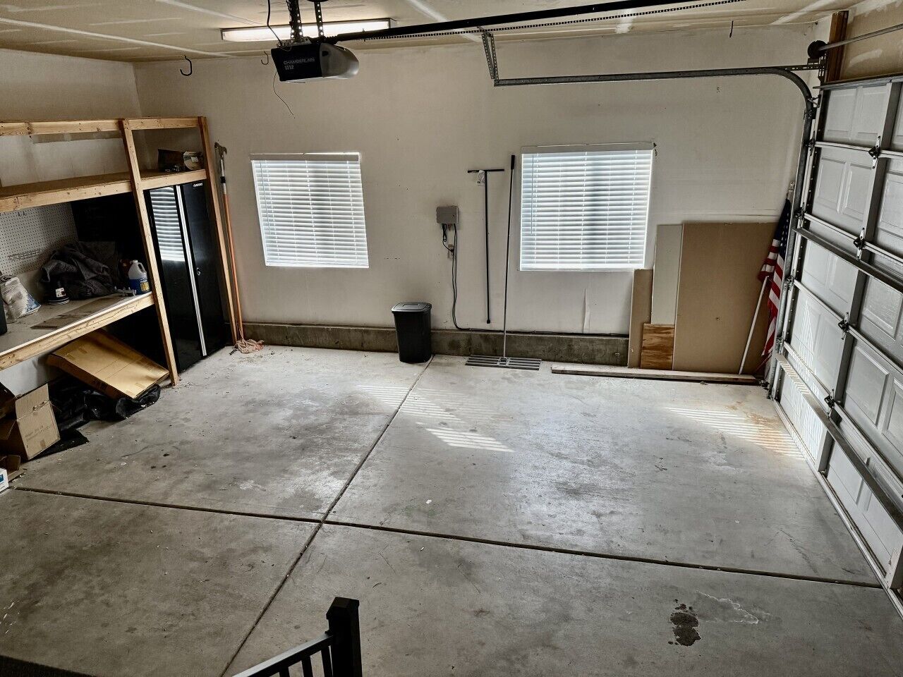 Eine Garage mit Betonboden, einer hölzernen Werkbank, einem schwarzen Kühlschrank und einer Garagentür.