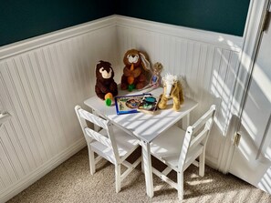 Habitación de esquina con una mesa y sillas blancas, un libro y peluches.