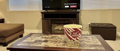 Una sala de estar con una televisión mostrando 'NETFLIX' y un cubo de palomitas de maíz en una mesa de centro.