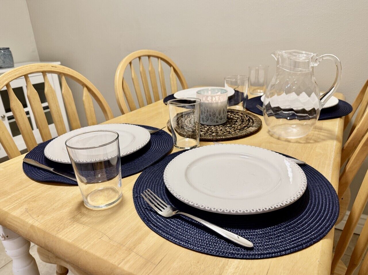 A dining table set with plates, cutlery, glasses, and a pitcher.