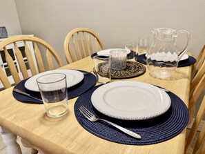 Una mesa de comedor dispuesta con platos, cubiertos, vasos y una jarrón.