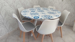 Una mesa de comedor redonda con mantel de estampado geométrico, rodeada por cuatro sillas blancas con cojines a cuadros blancos y negros.