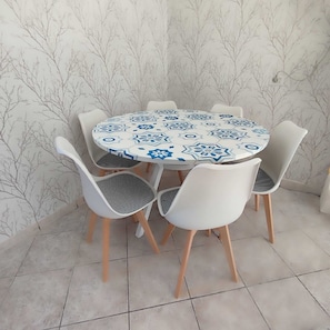 Una mesa de comedor redonda con mantel de estampado geométrico, rodeada por cuatro sillas blancas con cojines a cuadros blancos y negros.