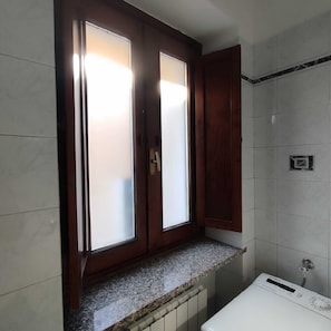 Un baño con ventana integrada, una encimera y una lavadora blanca.