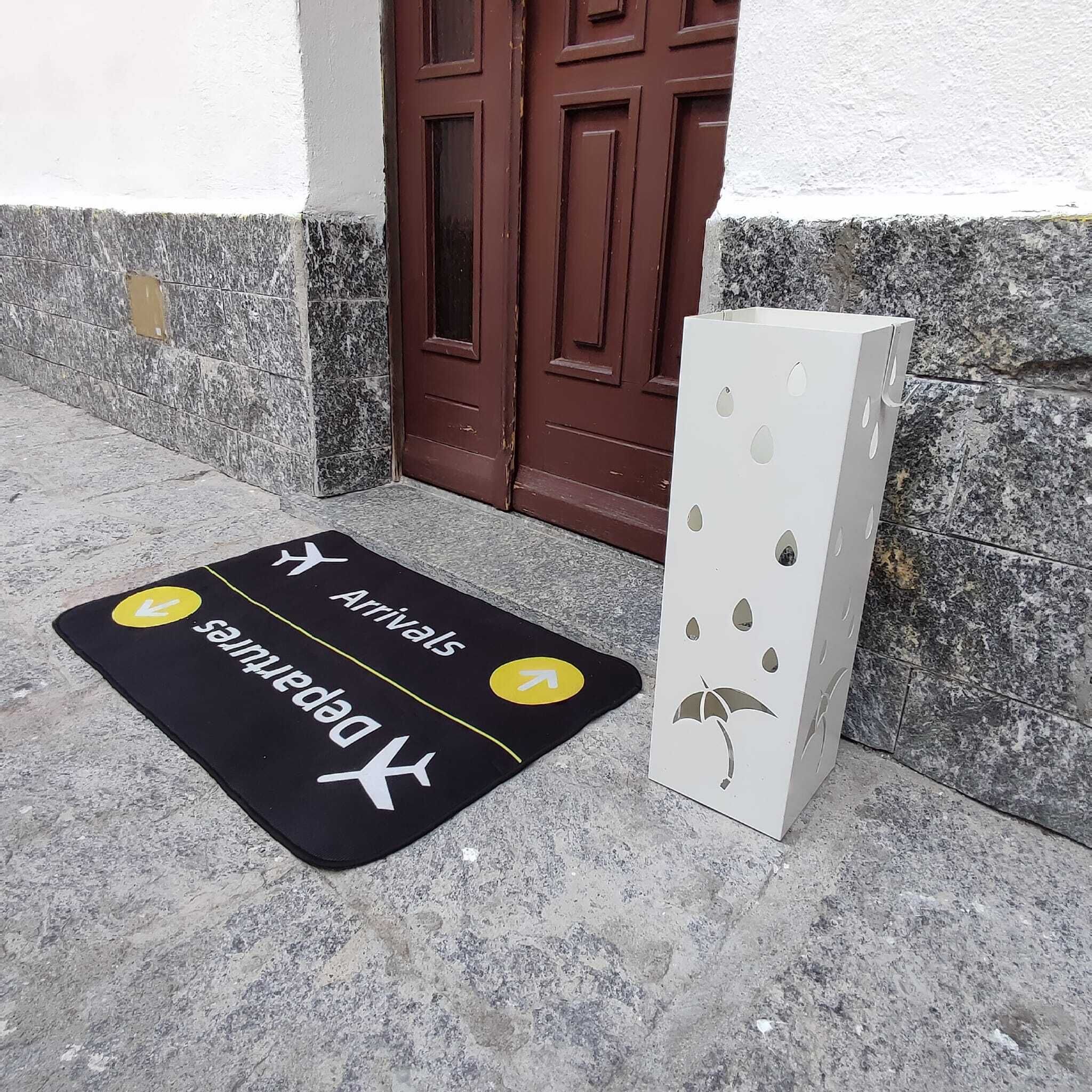 Un paillasson indiquant les directions « Arrivées » et « Départs », une porte marron et un objet blanc orné de motifs découpés.