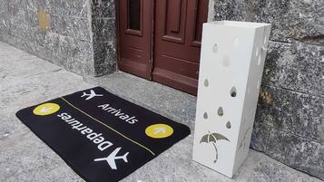 Un paillasson indiquant les directions « Arrivées » et « Départs », une porte marron et un objet blanc orné de motifs découpés.