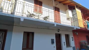 Un bâtiment à deux étages doté d’un balcon, d’une porte et d’un petit espace extérieur aménagé pour s’asseoir.
