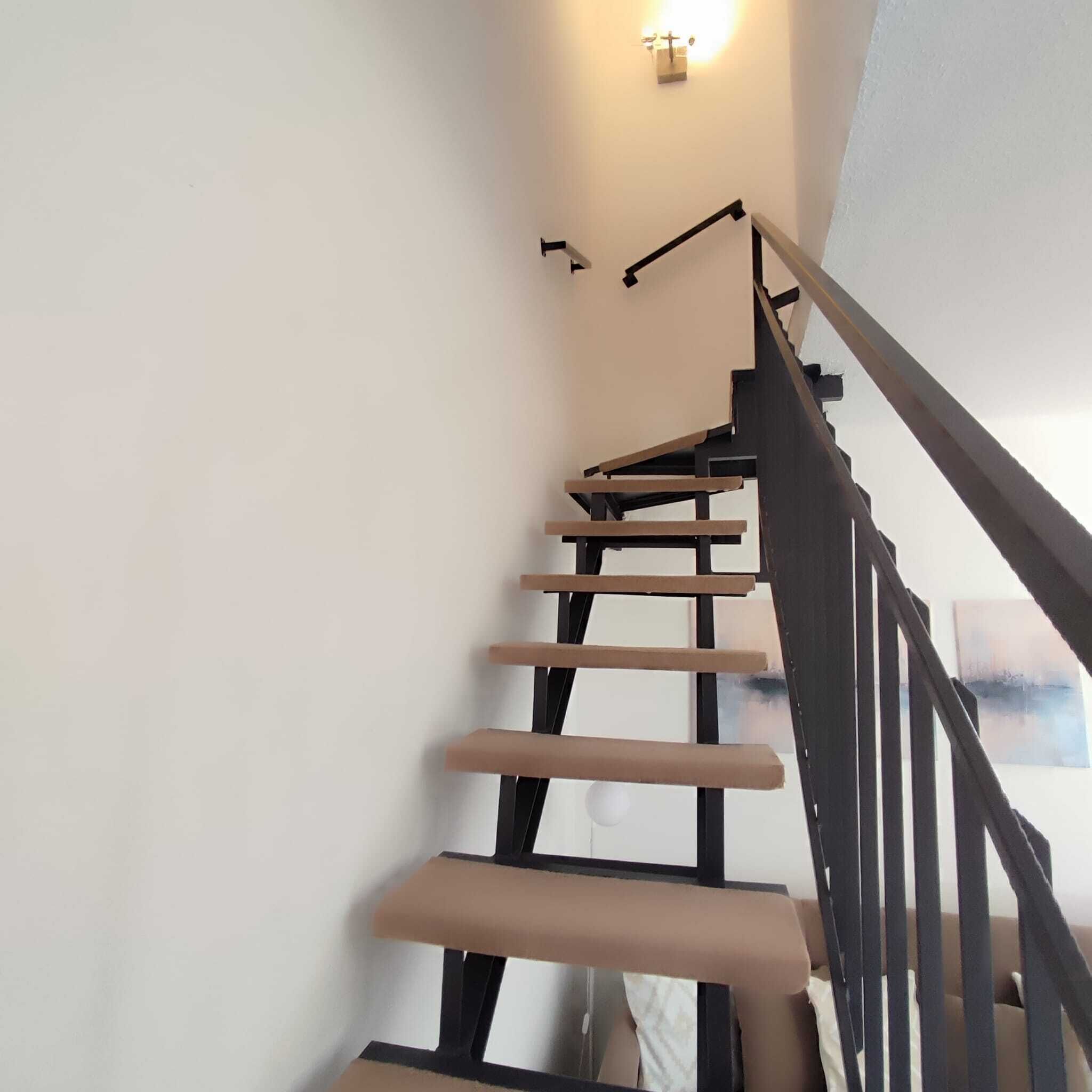 Un escalier avec une rampe en bois et un luminaire fixé au mur.