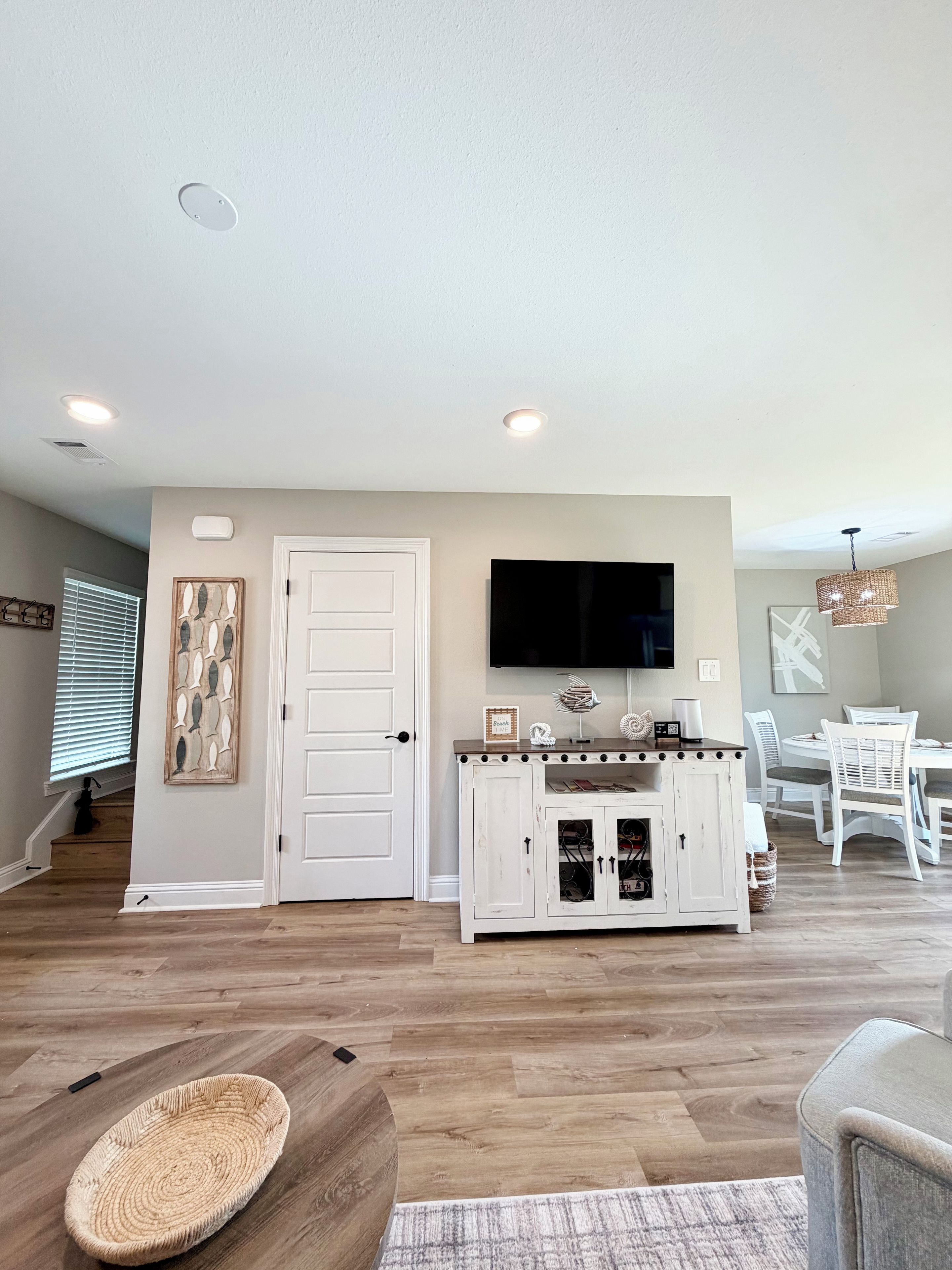 Una sala de estar con televisor de pantalla plana, un mueble blanco y un comedor con sillas blancas.