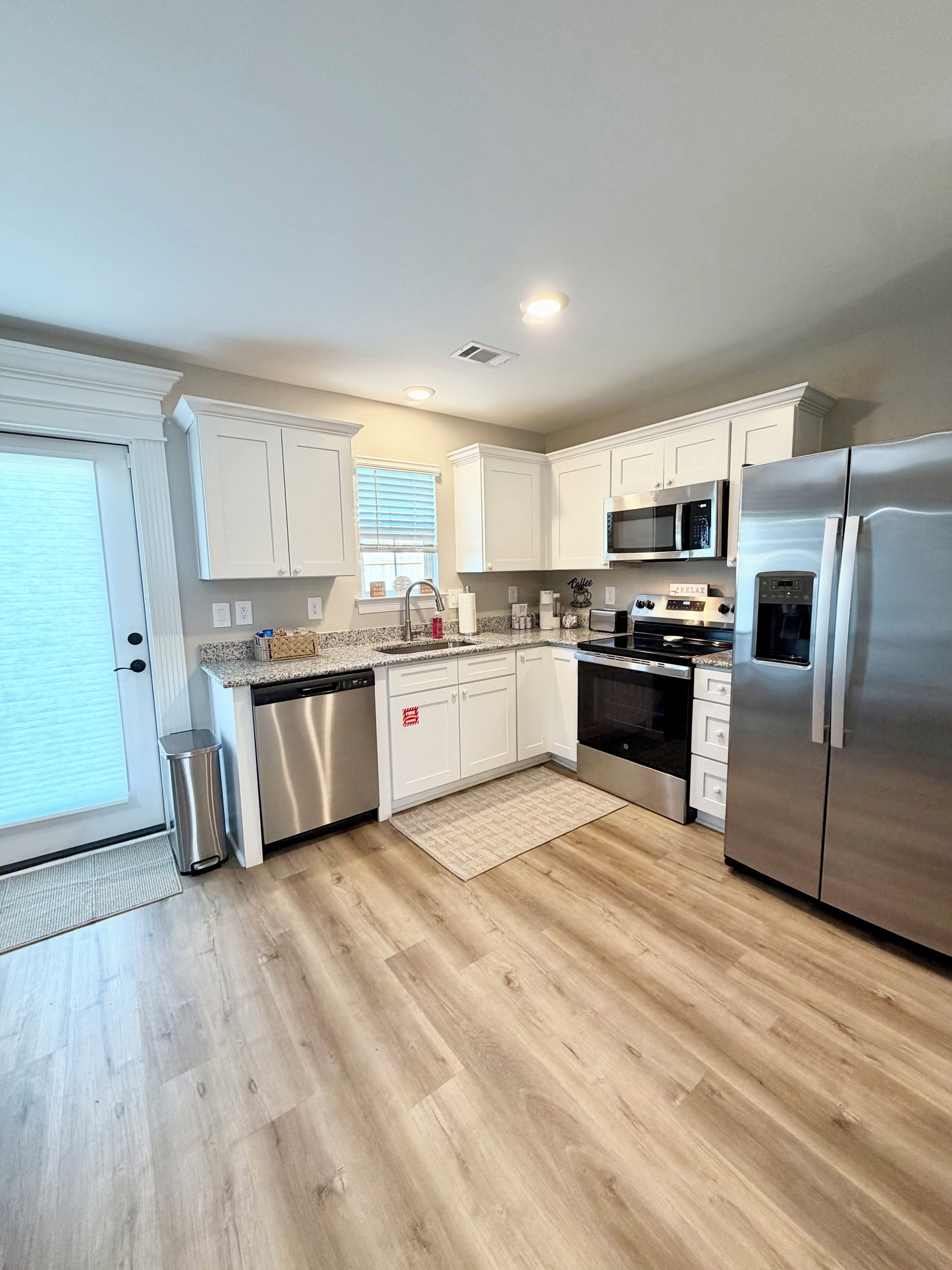 Una cocina moderna con armarios blancos, electrodomésticos de acero inoxidable y piso de madera.