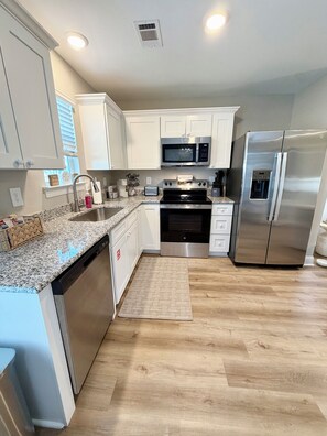 Una cocina moderna con armarios blancos, electrodomésticos de acero inoxidable, encimera de granito y suelo de madera.