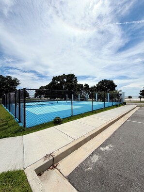 Ein von einer Zäunung umgebener Außenbereich mit blauer Fläche, möglicherweise ein Schwimmbad oder ein Sportplatz, neben einem Bürgersteig und einer Straße.