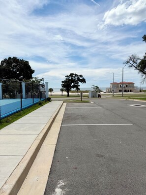 Un estacionamiento con una cerca azul, una acera y un edificio al fondo.