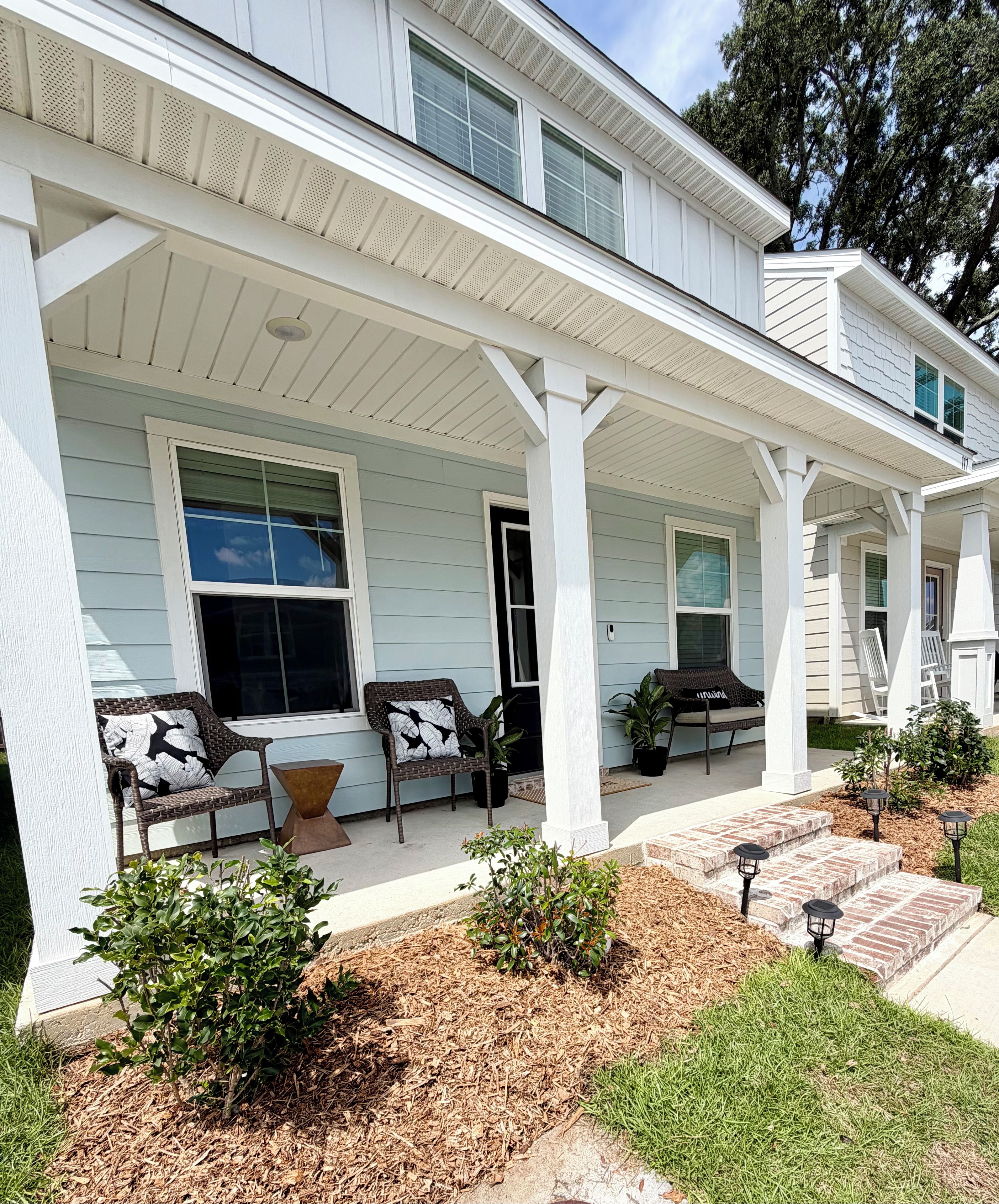 A two-story house with a covered porch, outdoor seating, and a landscaped garden.