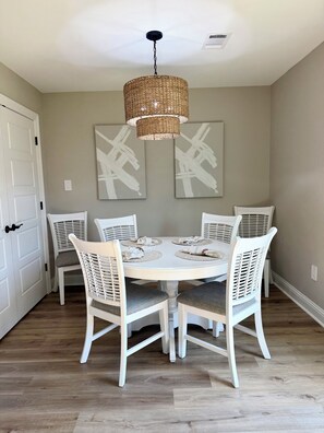 A dining area with a round table, white chairs, and a woven pendant light. - Gone Coastal •Steps to Beach •Pickleball •Heart of Biloxi (Biloxi)