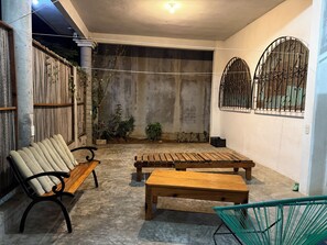 A covered outdoor seating area with benches and a chair, surrounded by a concrete floor and a wooden fence. - Conner House (Brisas de Zicatela)