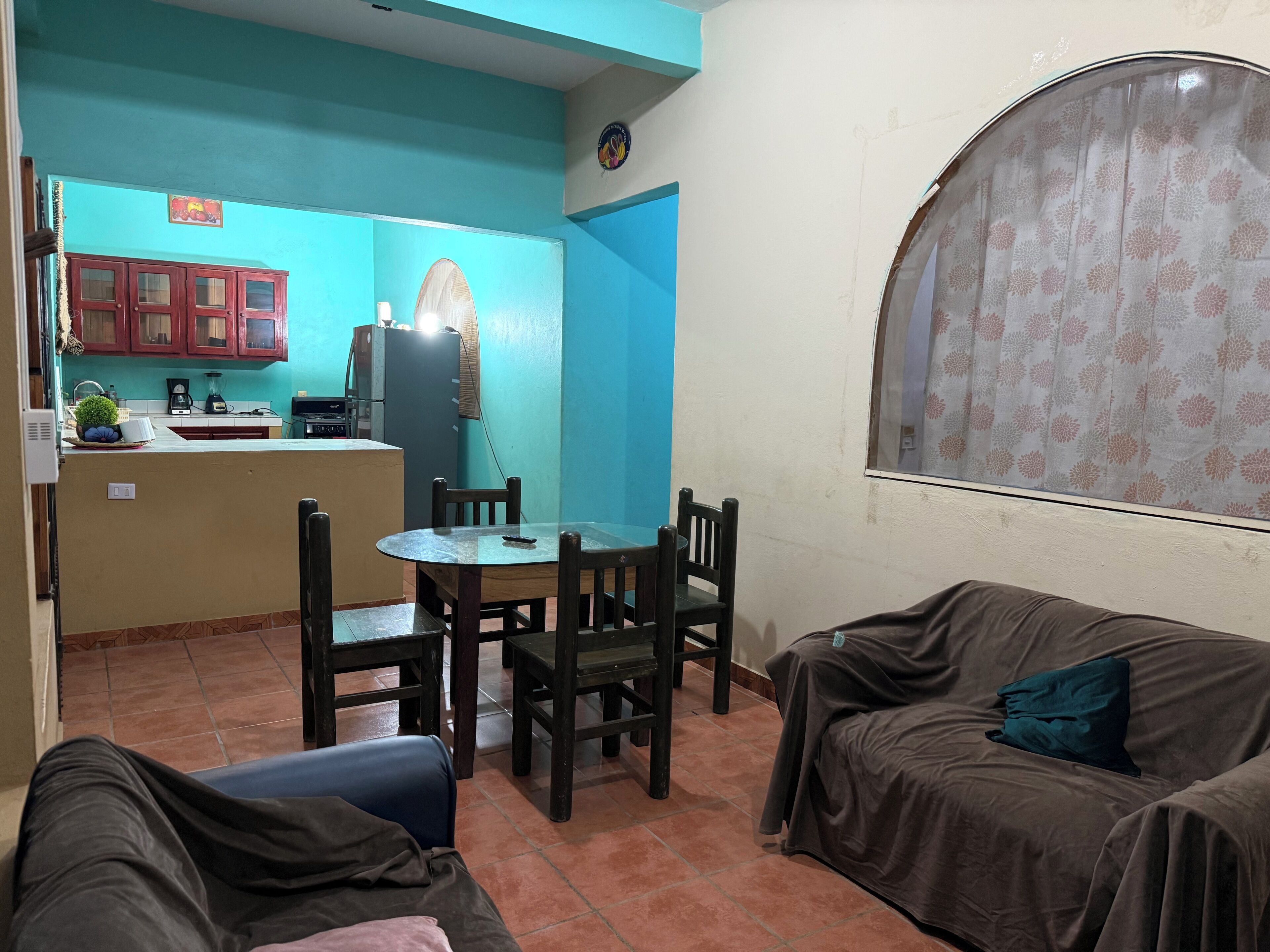 A living room with a dining area, a sofa, a table, and a kitchen in the background.