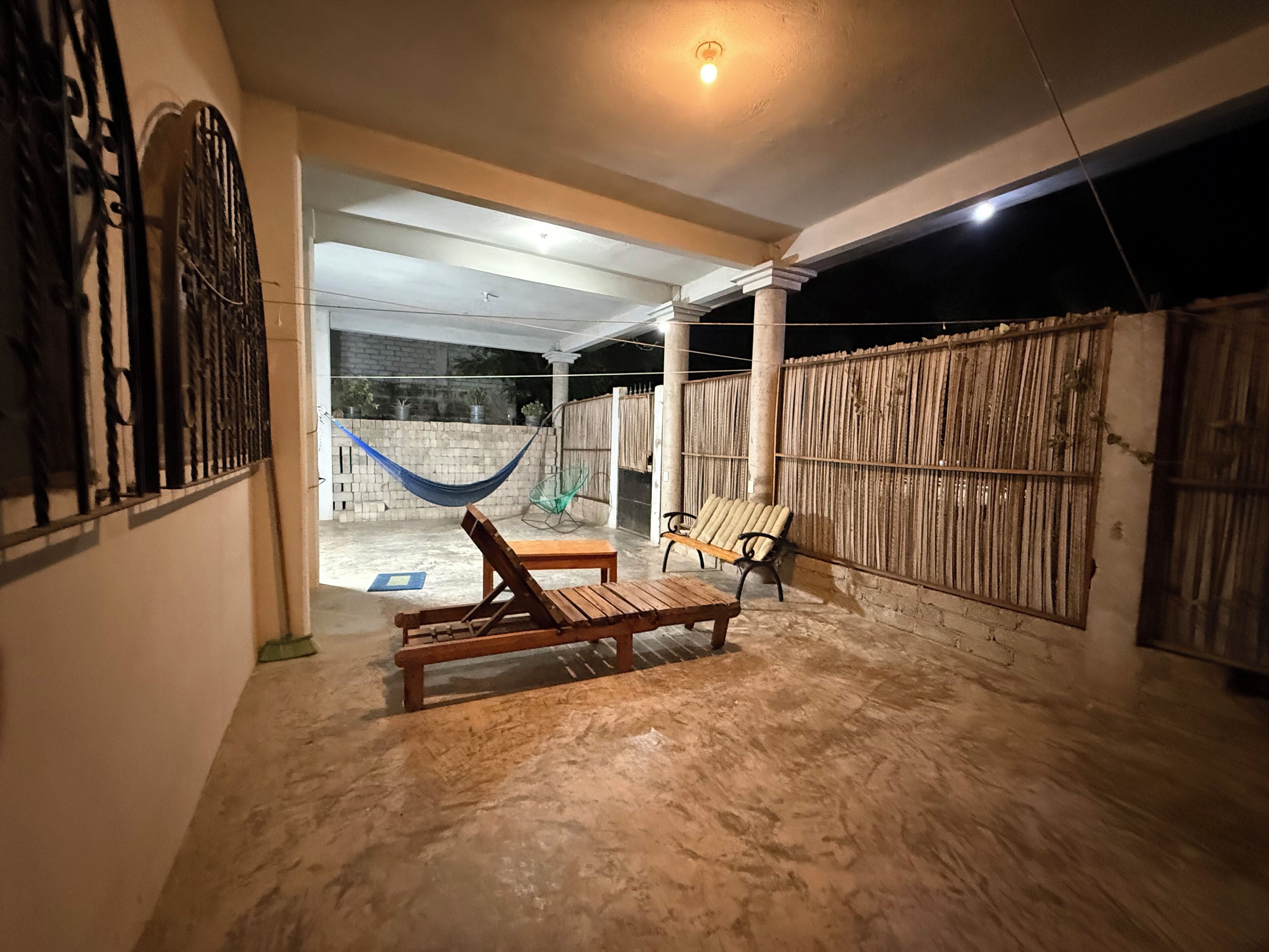 An outdoor patio area with a hammock, wooden lounge chairs, and a concrete floor.
