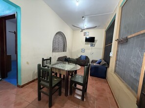 A dining area with a round table and chairs, a ceiling fan, a TV mounted on the wall, and a window with a curtain. - Conner House (Brisas de Zicatela)