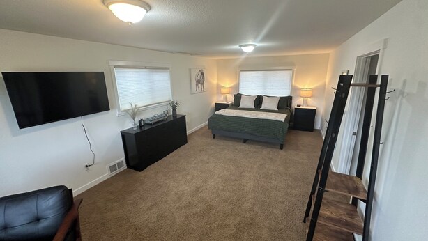 Un dormitorio con cama, mesitas de noche, cómoda, televisor y escalera.