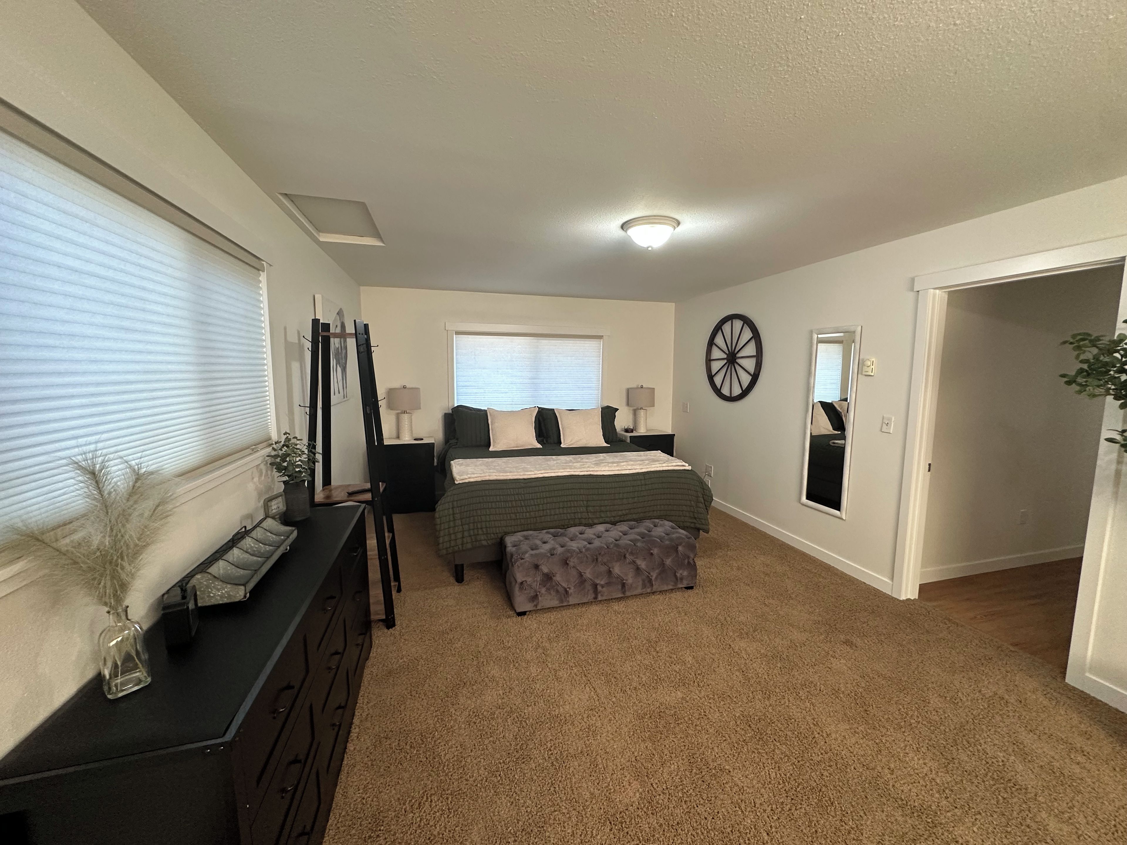 A bedroom with a bed, bedside tables, a dresser, a mirror, and a window with blinds.