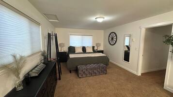 A bedroom with a bed, bedside tables, a dresser, a mirror, and a window with blinds.