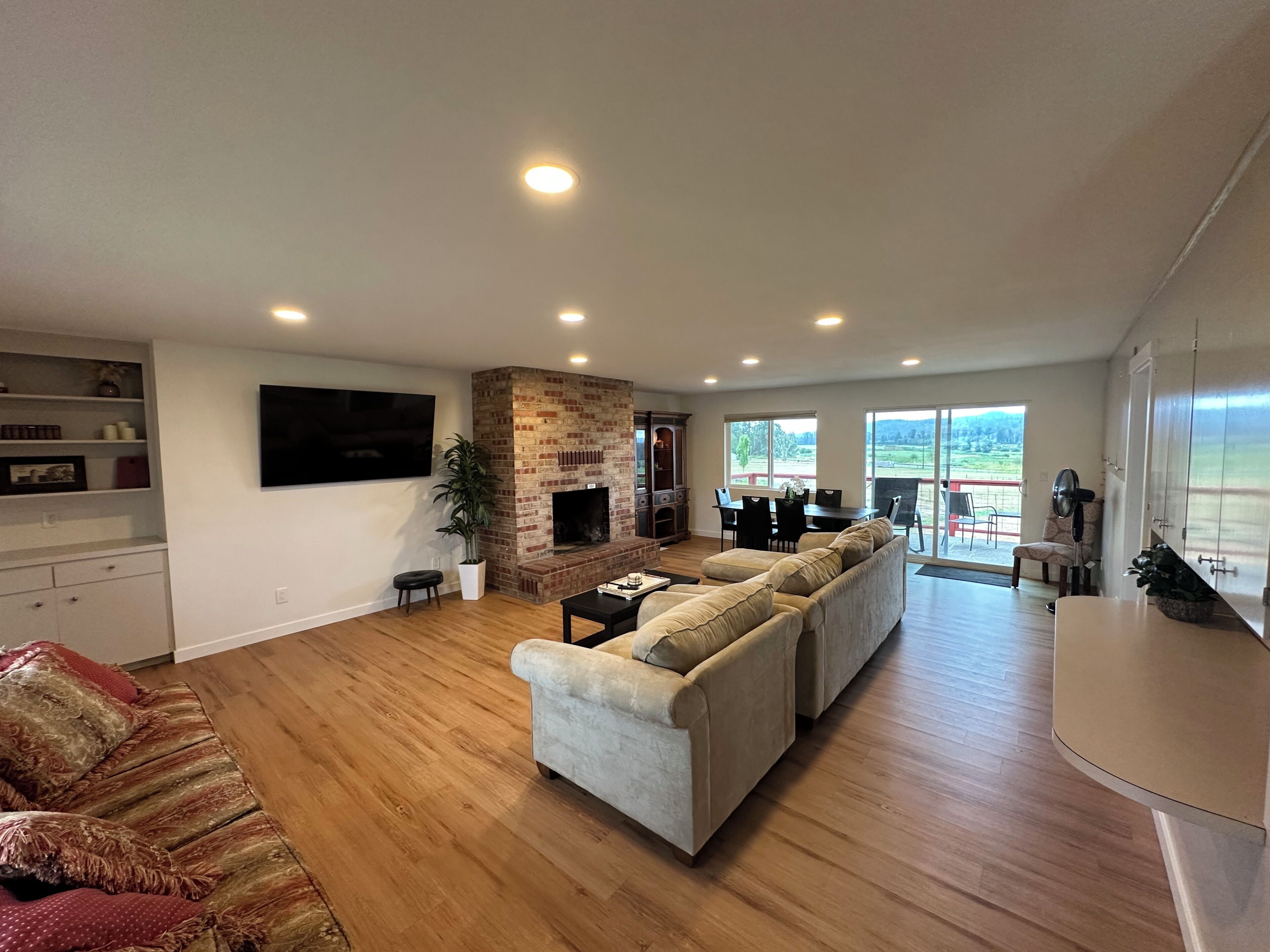 A spacious living room with a fireplace, a large sofa set, a flat-screen TV, and a dining area with a view of the outdoors.