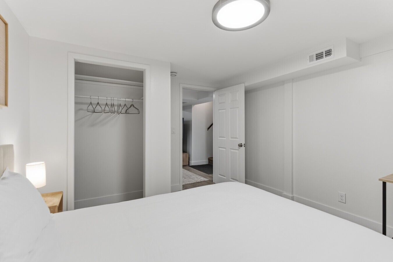 Un dormitorio con cama, un armario con ropa colgada y una puerta que da a otra habitación.