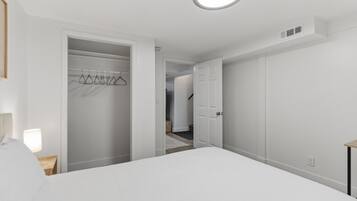 A bedroom with a bed, a closet with hanging clothes, and a door leading to another room.