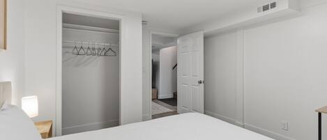 Un dormitorio con cama, un armario con ropa colgada y una puerta que da a otra habitación.